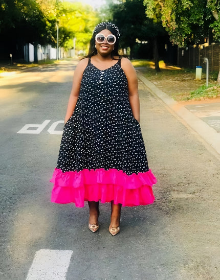 Black polka dot maxi dress with sleeveless bodice and bright pink ruffle hem