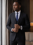 Men's slim-fit formal suit, dark blazer and matching trousers, side stance.