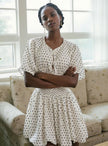 White polka dot mini dress with a smocked waist, short sleeves, and a V-neckline, shown on a model.
