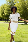 Ensemble pull maille et jupe rayée blanche, col boutonné et bordures dorées.
