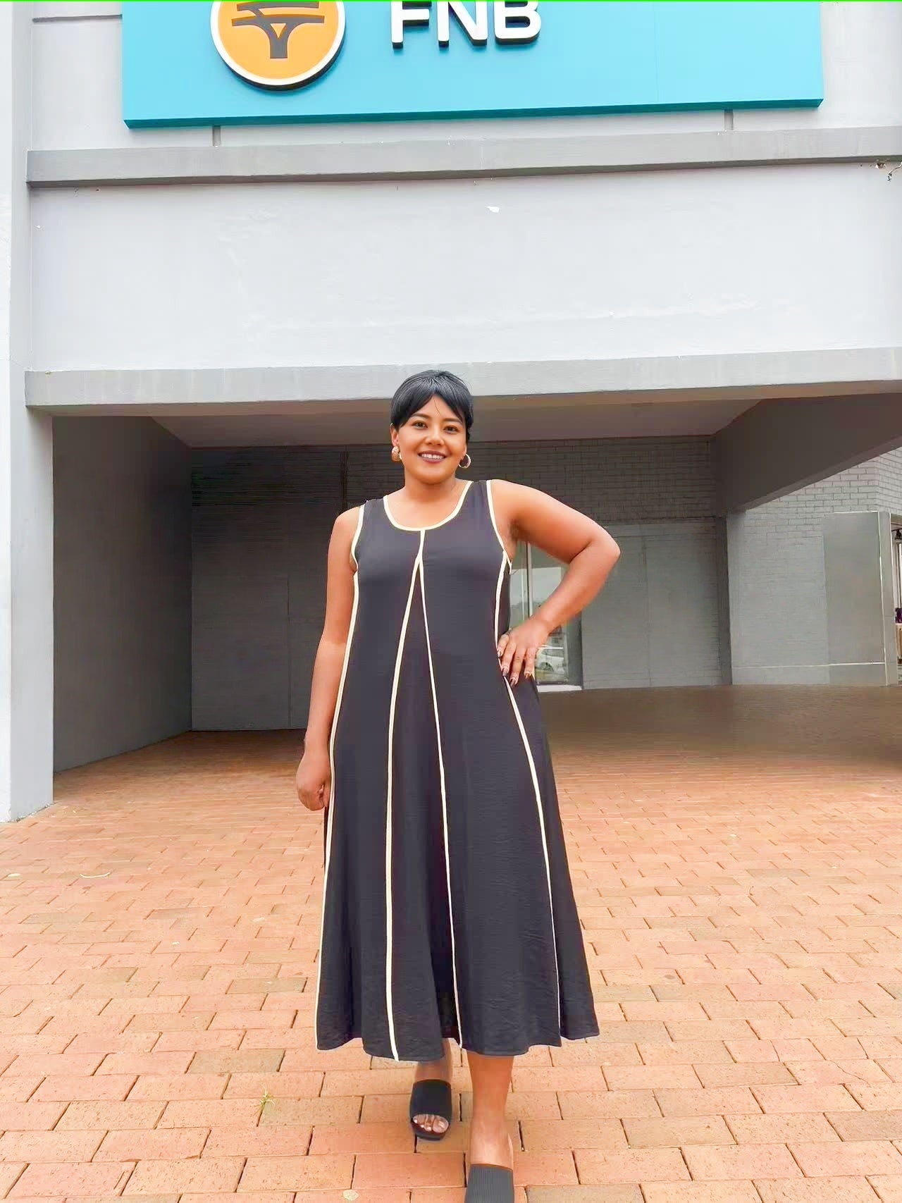 Black sleeveless A-line maxi dress with thin gold trim around the neckline and seams