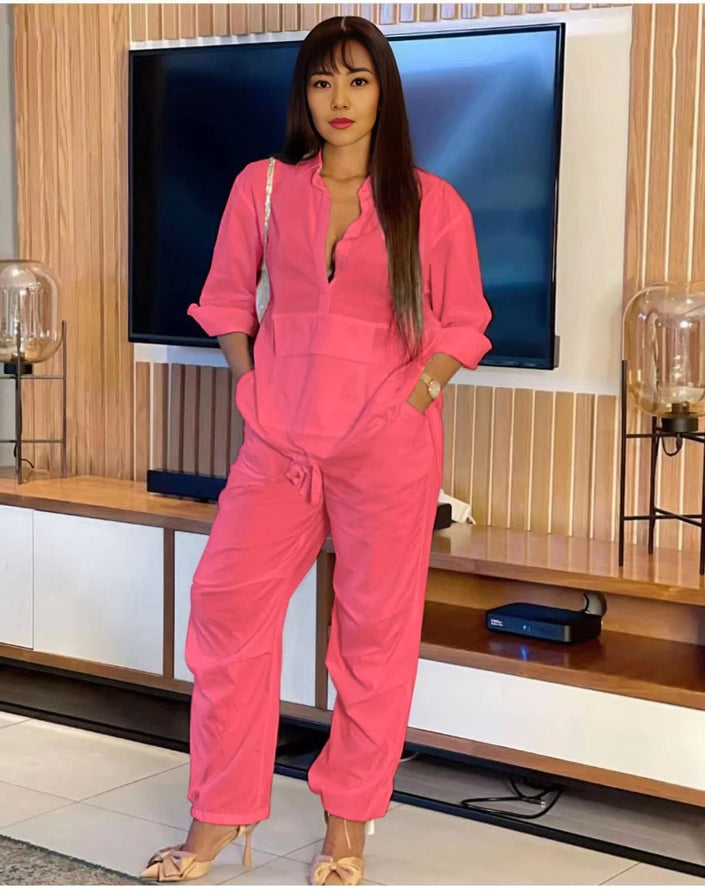 Pink solid color jumpsuit with long sleeves, V-neck, and adjustable waist ties