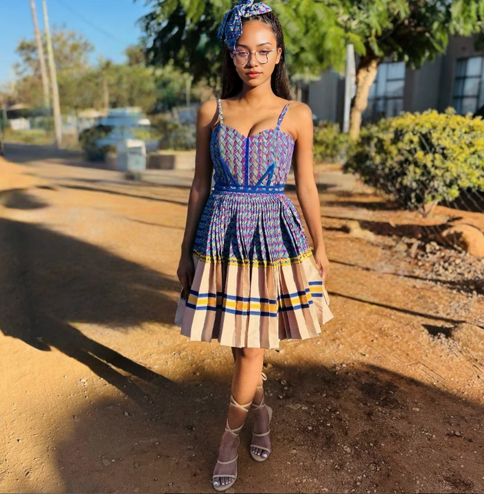 Ethnic mini dress with sleeveless square neckline, pleated patchwork skirt in blue and yellow.