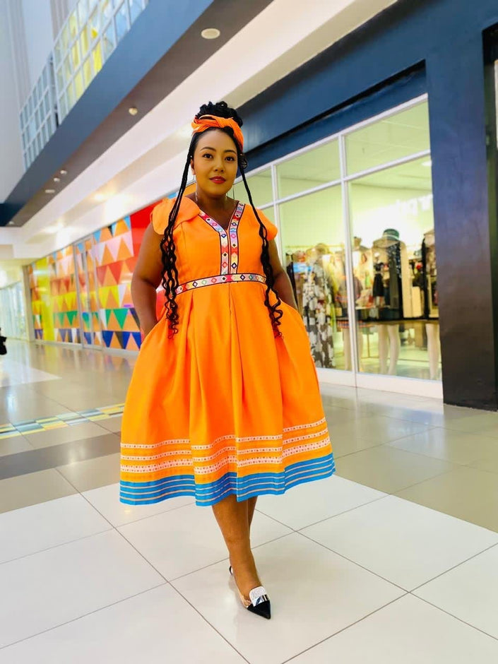 Orange maxi dress with puff sleeves, patterned neckline, and striped hem in blue and yellow