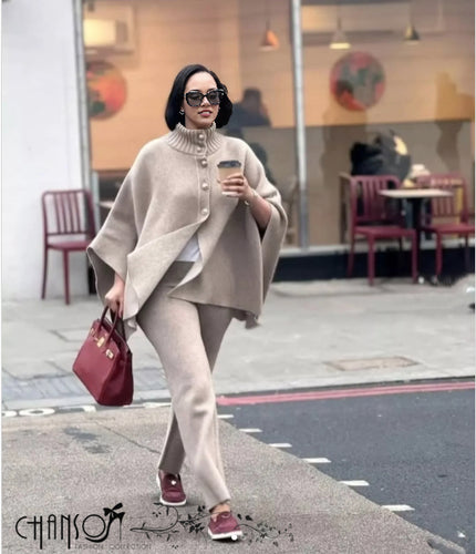 Beige knitted twin set cape with high neck and button front, draped over pants